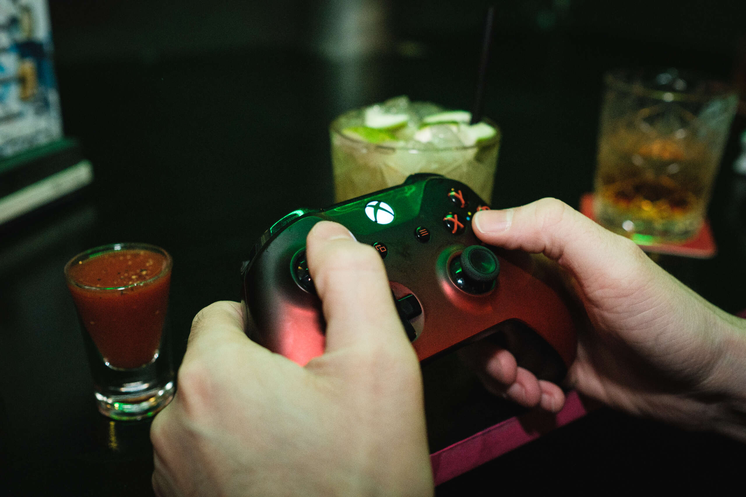 Person spielt an Xbox Controller, im Hintergrund ein Meikaner Shot und zwei Cocktails